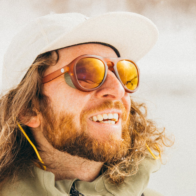 Man wearing a white hat and sunglasses with a beard, smiling outdoors.