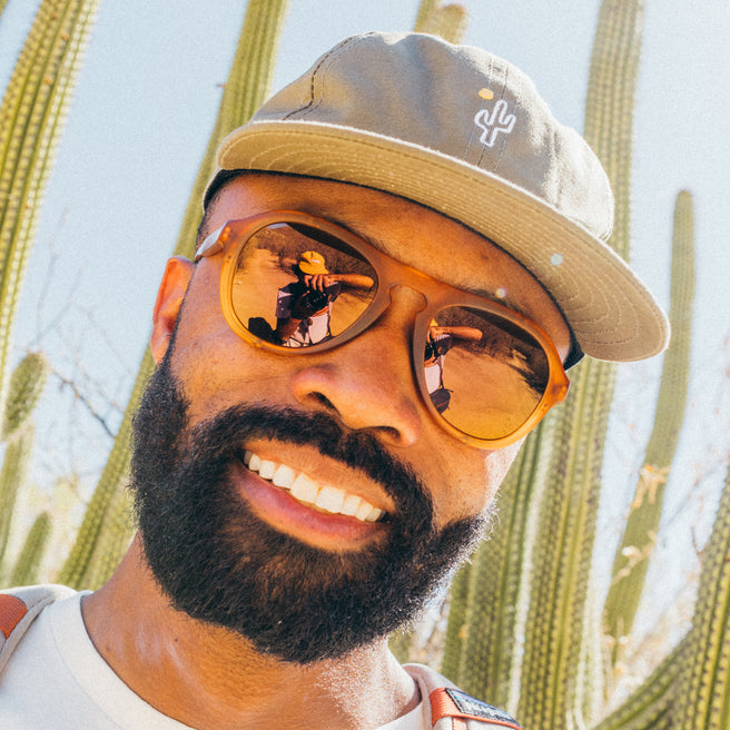 Man wearing sunglasses and a cap with cacti in the background
