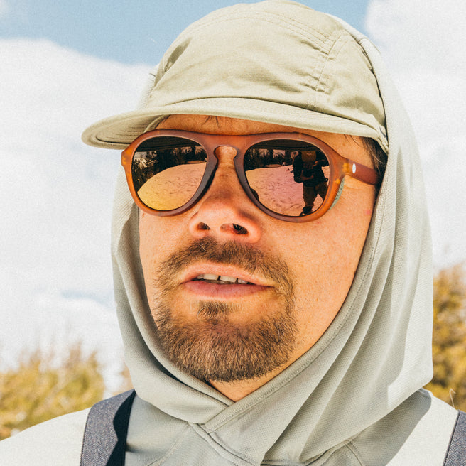 Man wearing a beige cap and sunglasses with a blurred natural background