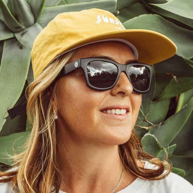 Woman wearing a yellow cap and sunglasses with a green leafy background