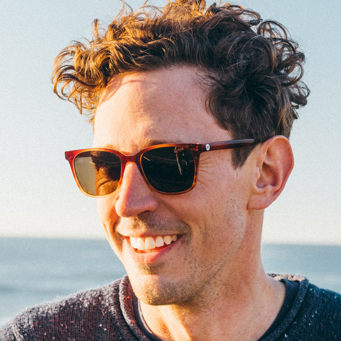 Man wearing sunglasses with a blurred background of water and sky