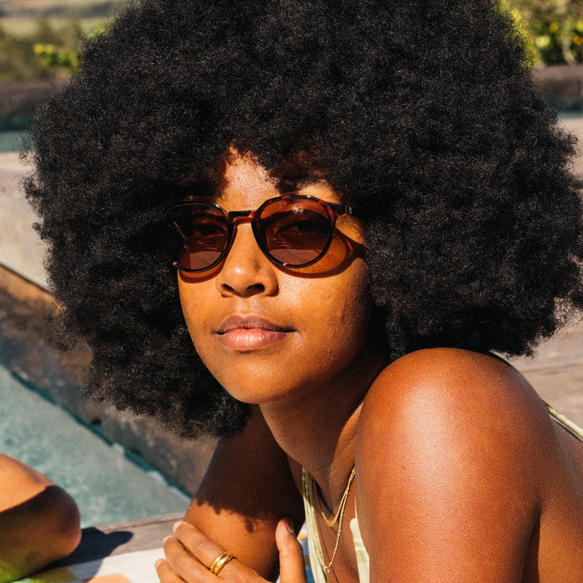 Woman with an afro wearing sunglasses by a pool