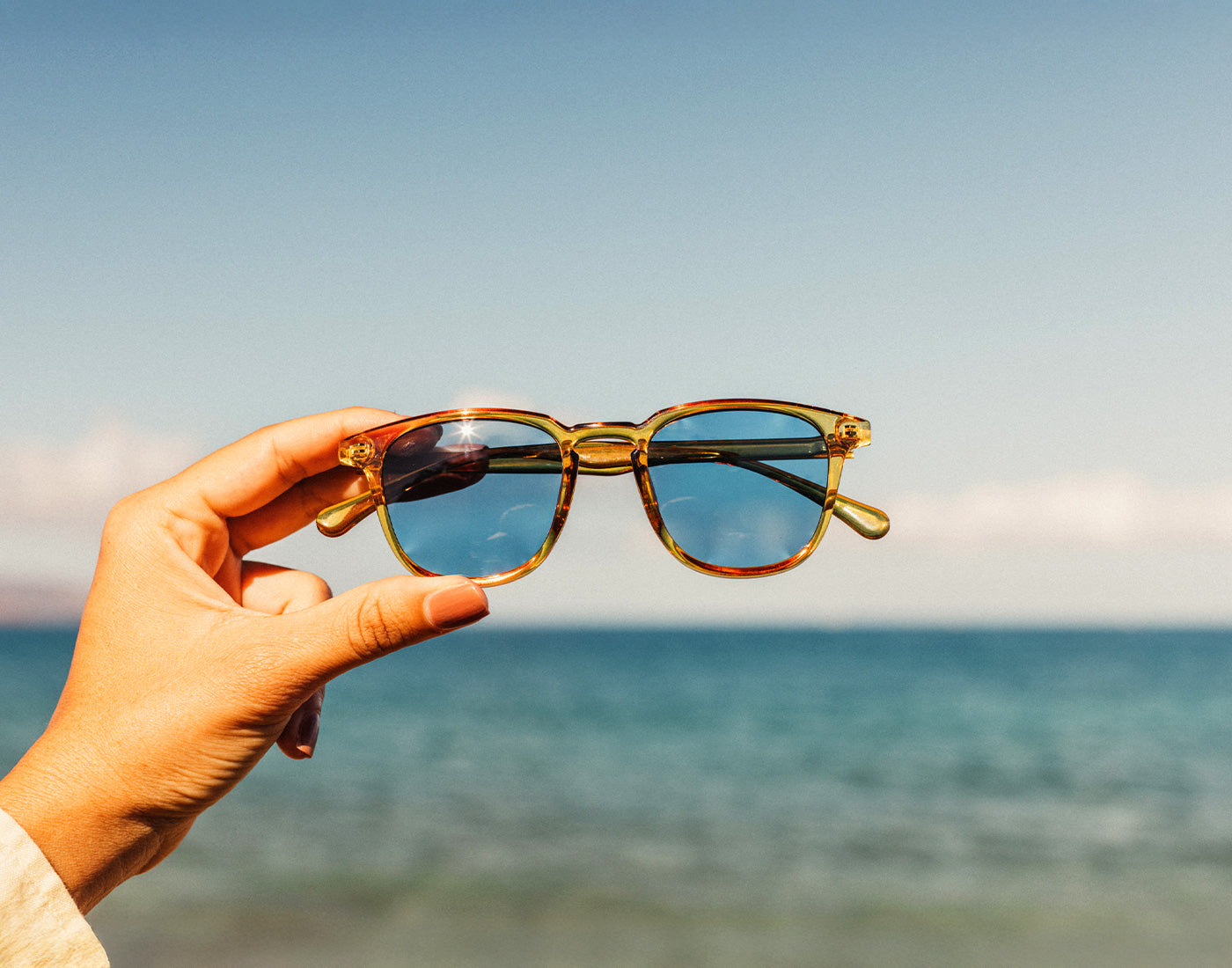 hand holding sunski tango sunglasses over ocean