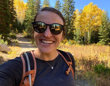 Person with sunglasses and backpack standing in a forest with autumn foliage