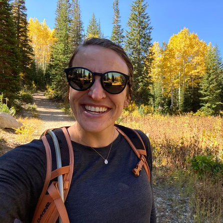 Person with sunglasses and backpack standing in a forest with autumn foliage
