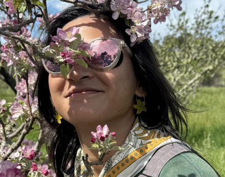 Person with sunglasses and floral hair standing among cherry blossom trees