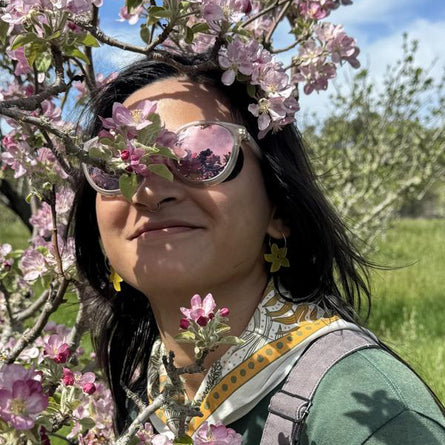 Person with sunglasses and floral hair standing among cherry blossom trees