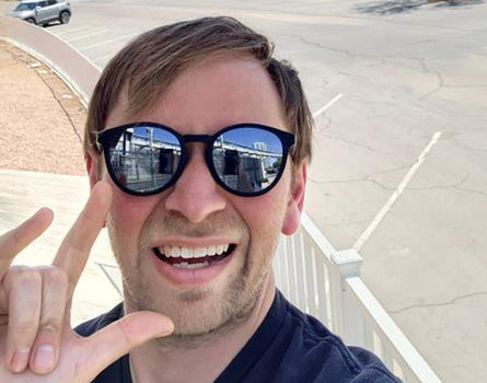 Man wearing sunglasses with a parking lot and cars in the background