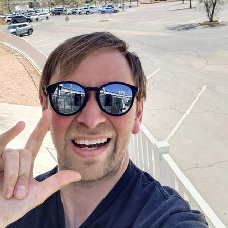 Man wearing sunglasses with a parking lot and cars in the background