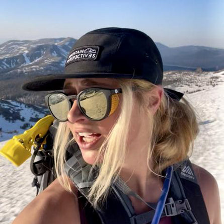 Person on a snowy mountain with goggles and a cap, with mountains in the background