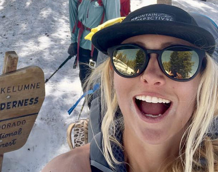 Person with a backpack and sunglasses in a snowy landscape near a sign.
