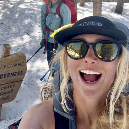 Person with a backpack and sunglasses in a snowy landscape near a sign.