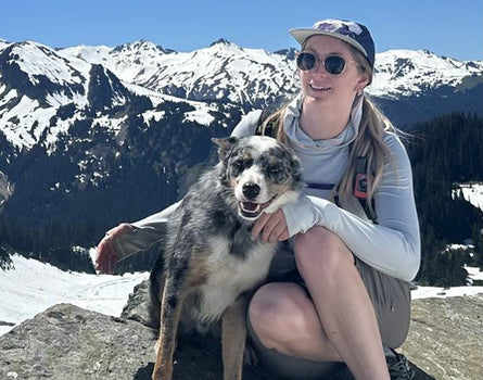 Woman and dog sitting on a rock with snow-capped mountains in the background