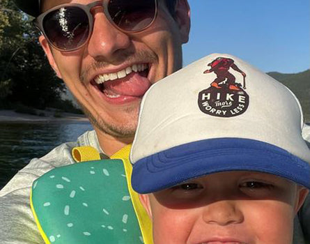 Man and child smiling outdoors with a scenic background