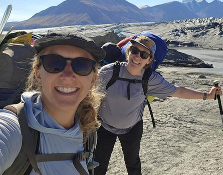 Two hikers taking a selfie on a mountain with backpacks and sunglasses.