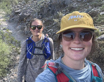 Woman wearing yellow hat and sunglasses hiking with a friend in the mountains