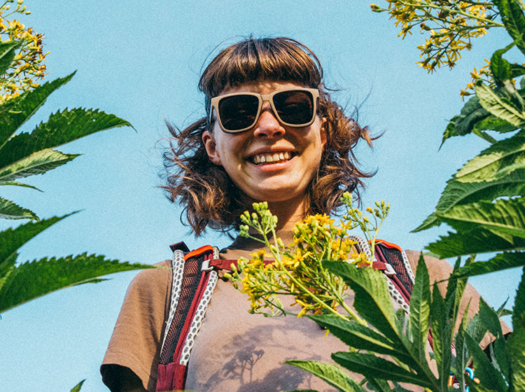 Person with sunglasses standing among plants with a clear blue sky background