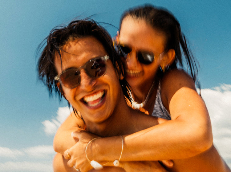 Two people wearing sunski sunglasses with a clear blue sky background