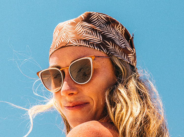 woman wearing sunski catalina sunglasses and a patterned headband against a clear blue sky