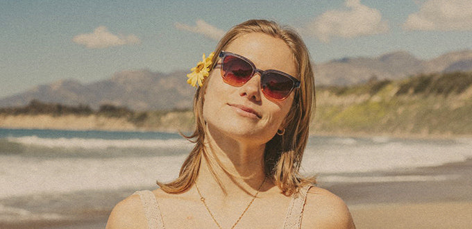 woman at the beach in sunski sunglasses with flower in hair
