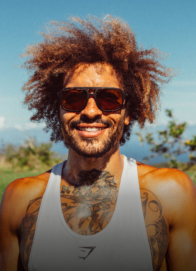 Man with tattoos wearing sunglasses and a tank top outdoors
