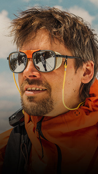 Man wearing sunglasses with a reflective surface, outdoors with a blurred natural background
