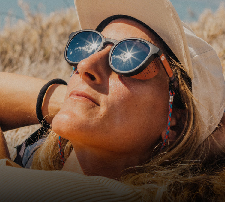 Person wearing a wide-brimmed hat and sunglasses with reflective lenses outdoors.