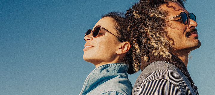 Two people wearing sunglasses against a clear blue sky