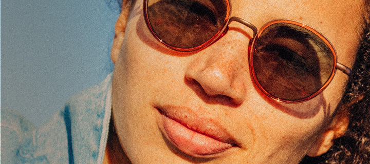 Close-up of a person wearing round sunglasses with a blurred blue background