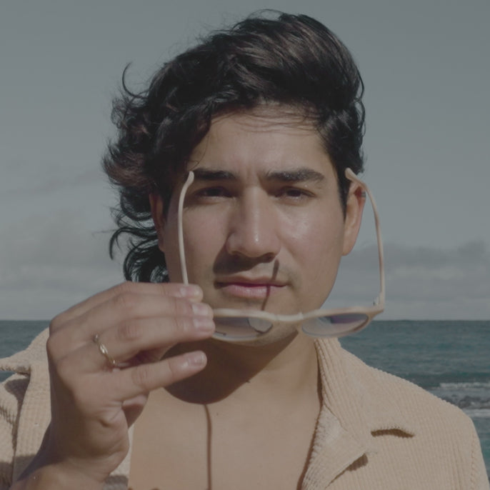 a man with hair blowing in the breeze trying on sunglasses