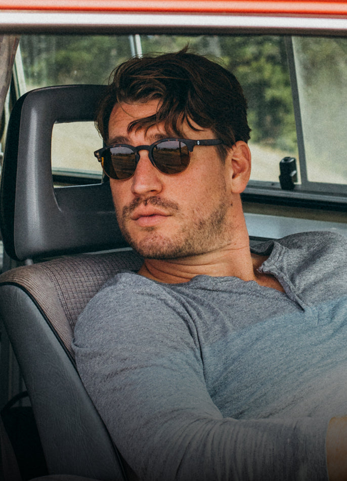 Man wearing sunglasses sitting inside a car with a blurred outdoor background