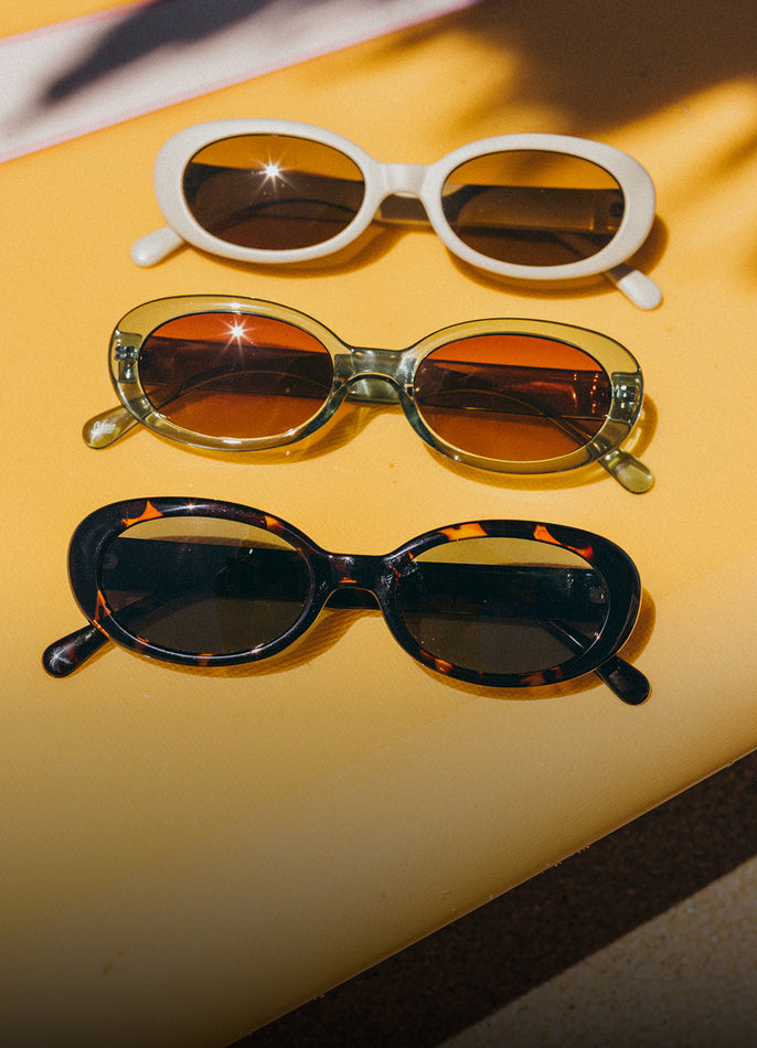 Three pairs of sunglasses on a yellow surface with shadows.