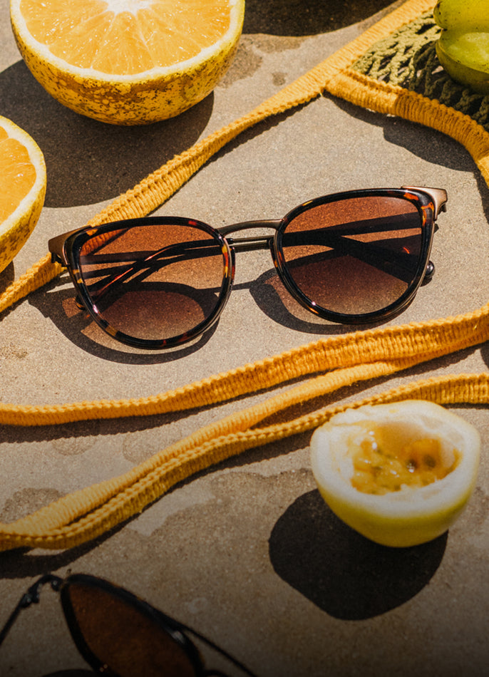 Sunglasses with a yellow strap on a textured surface with sliced oranges and a boiled egg.
