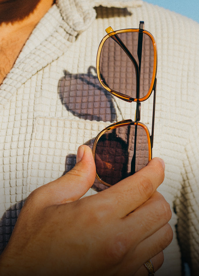 Hand holding a pair of sunglasses with a textured white garment in the background