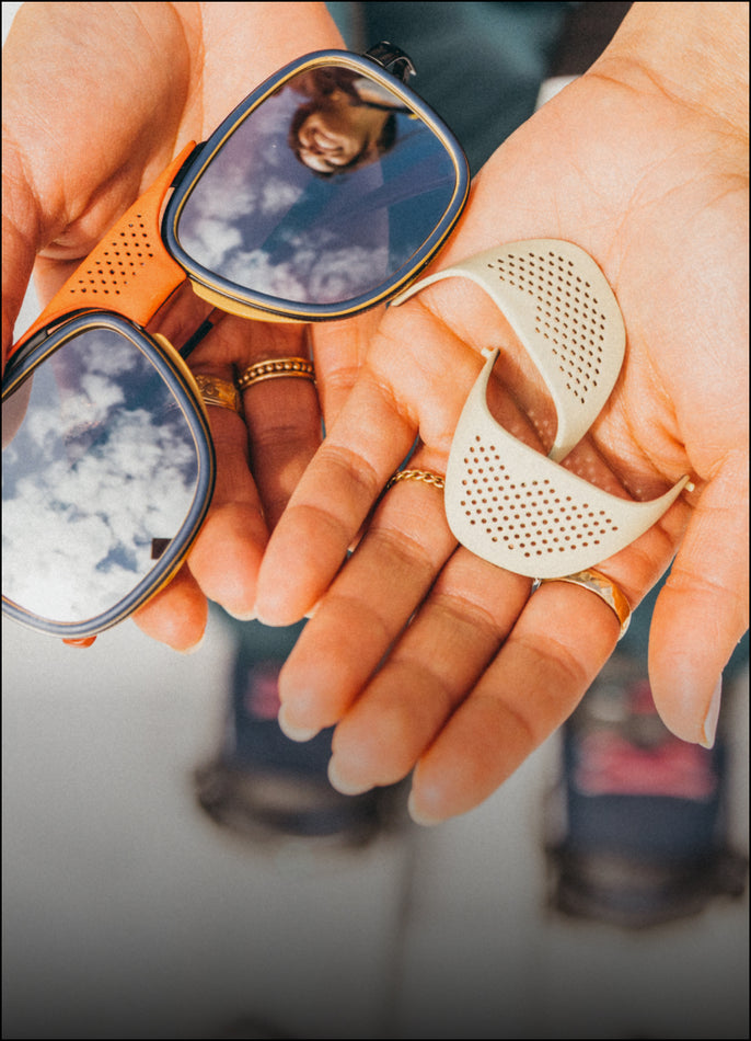 Close-up of hands holding a pair of sunglasses with orange frame and beige lenses.