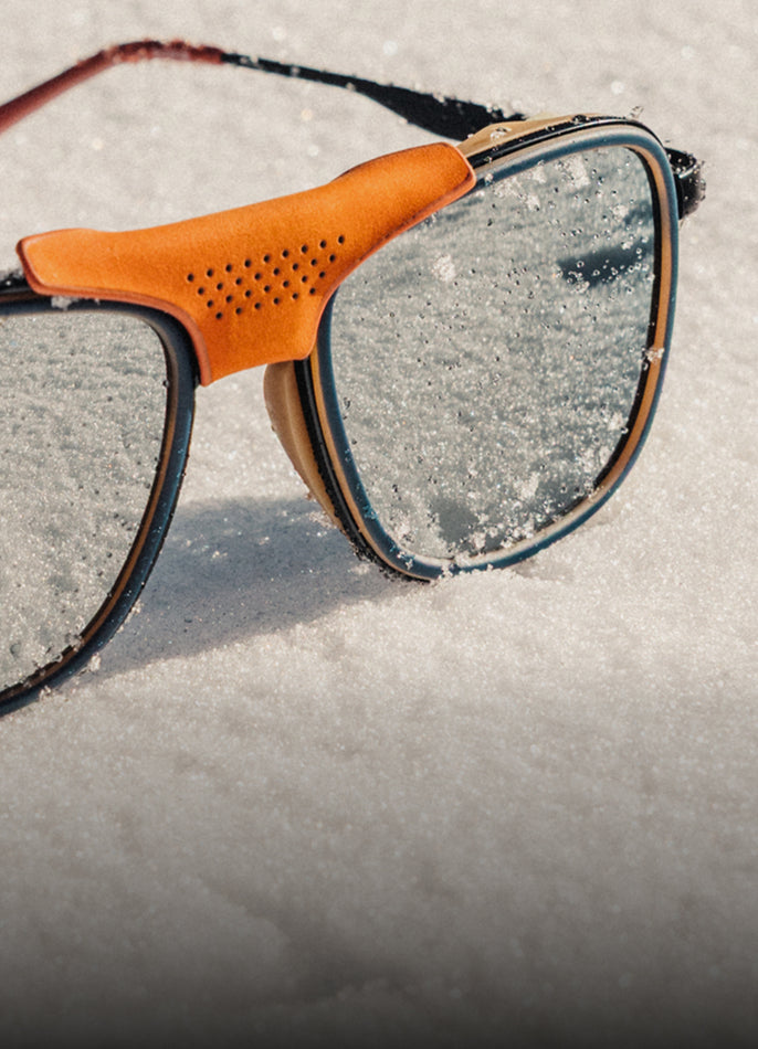 Sunglasses with orange frame and reflective lenses on a sandy surface