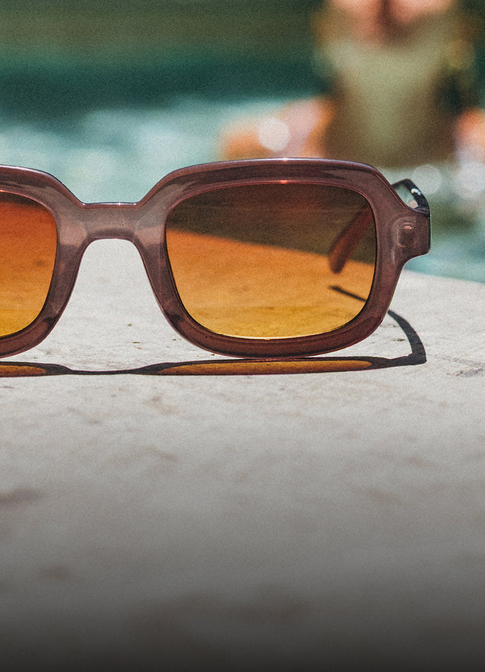 Brown sunglasses with reflective lenses on a concrete surface near water.