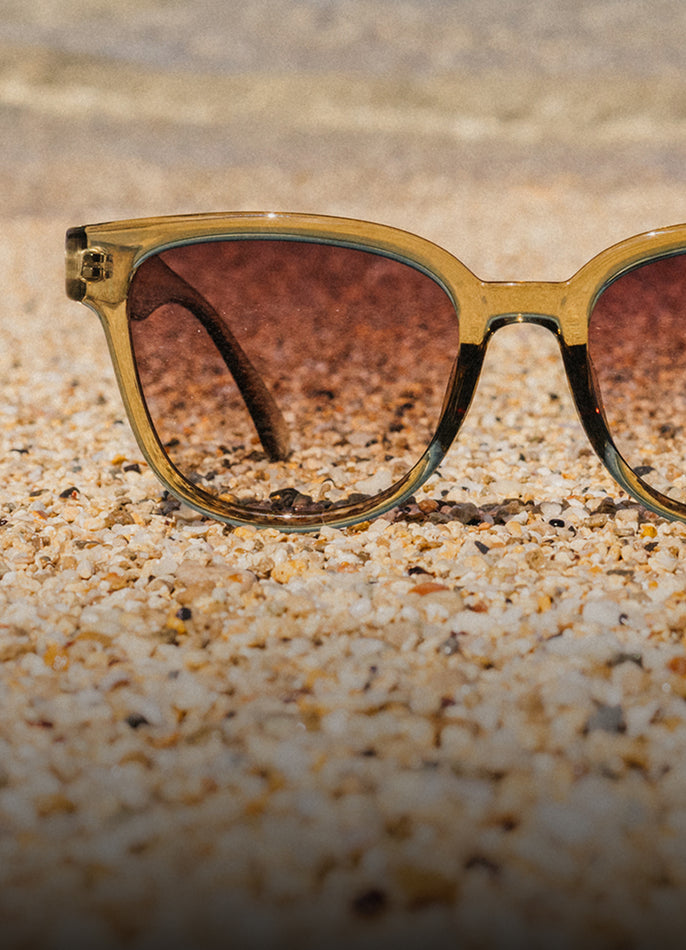 Sunglasses with a gold frame and brown lenses on a sandy surface