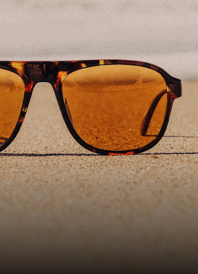 Sunglasses with tortoiseshell frame and amber lenses on a textured surface