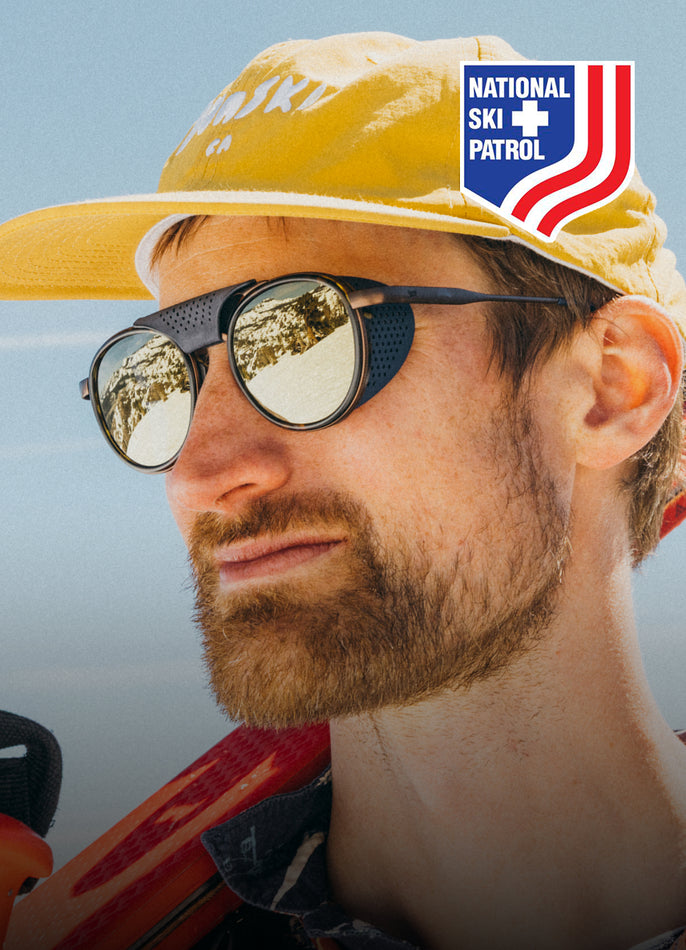 Person wearing a yellow National Ski Patrol hat with sunglasses and a blue sky background