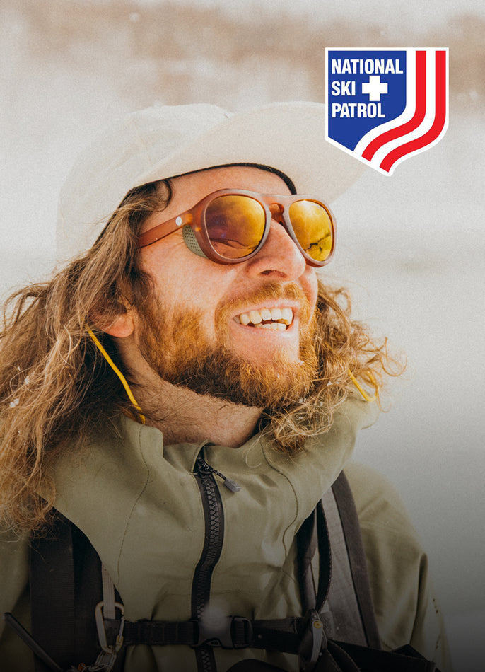 Person wearing sunglasses and a helmet with National Ski Patrol logo in the background