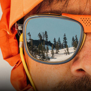 Person wearing orange goggles with a snowy landscape reflection, wearing an orange jacket.