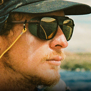 Close-up of a person wearing sunglasses and a cap with a blurred natural background