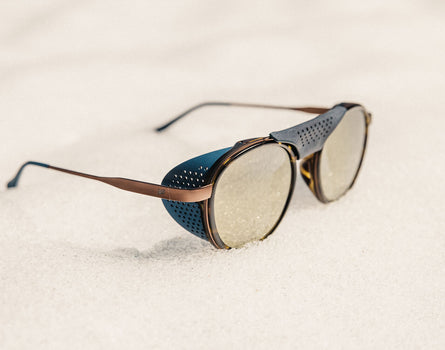 Sunglasses with a blue case on a sandy surface