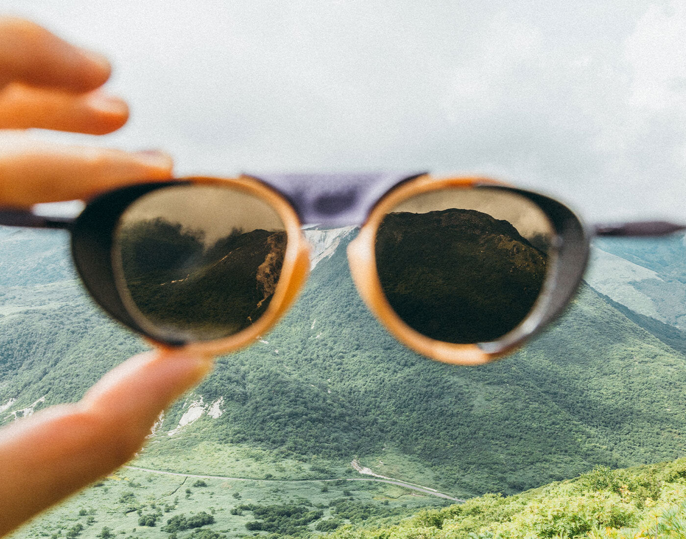 Sunglasses with mountain reflection held up to a scenic view of mountains and sky.