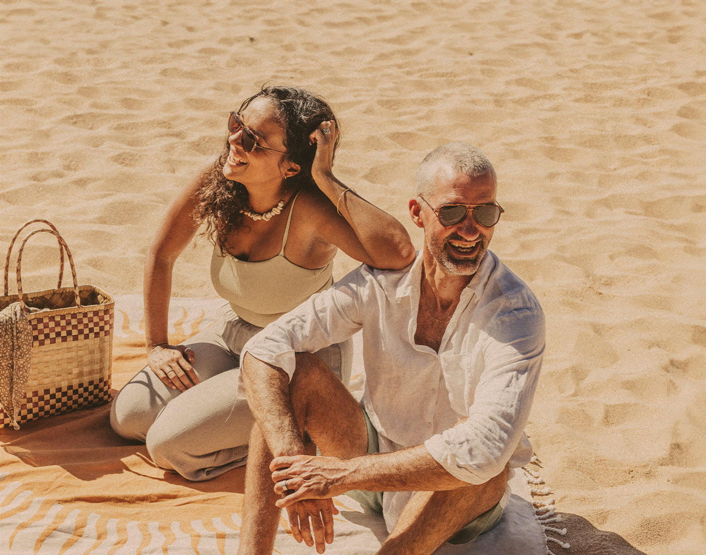 man and woman sitting on the beach wearing sunski astra sunglasses
