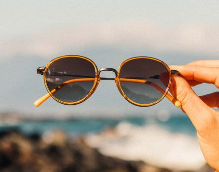 hand holding sunski baia sunglasses by the beach