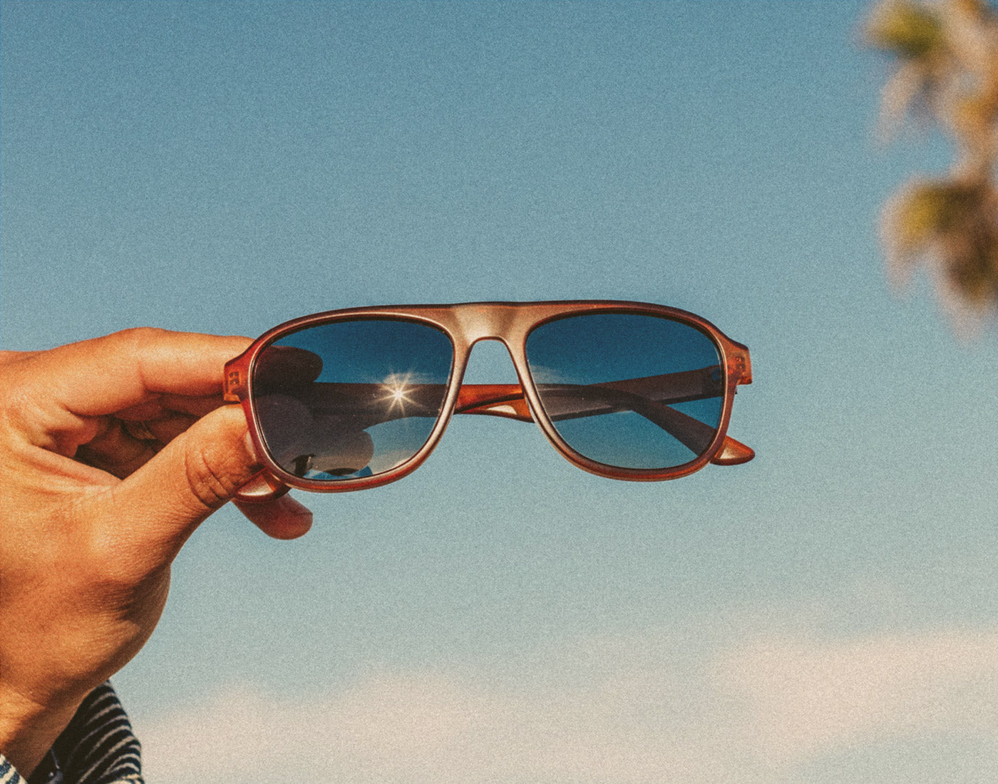 hand holding sunski shoreline sunglasses in front of blue sky 