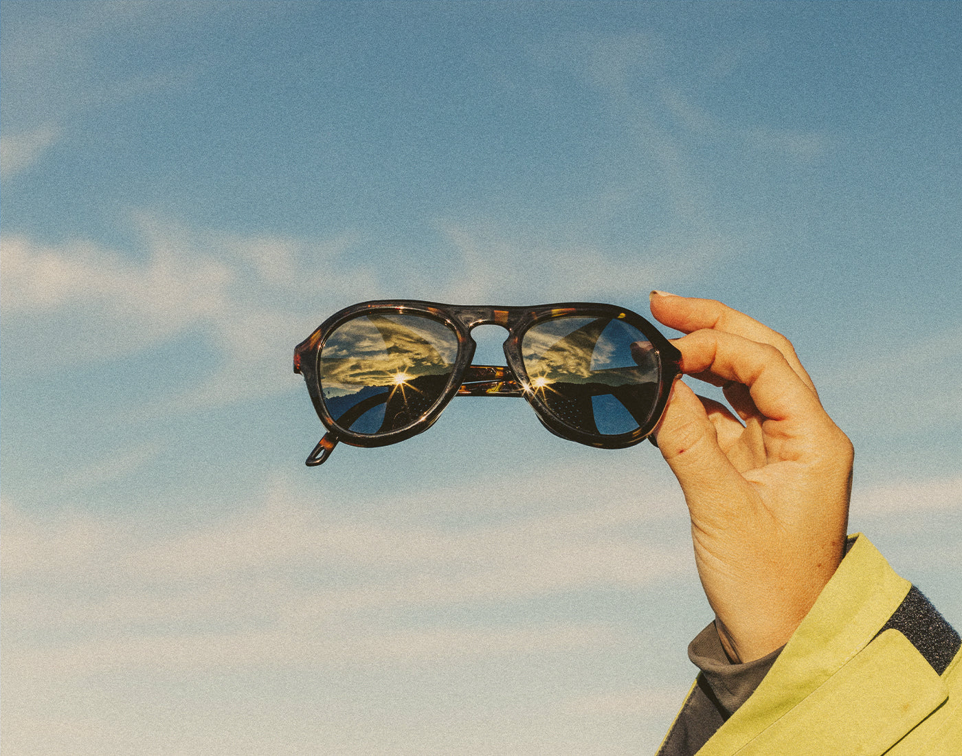 hand holding sunski treeline sunglasses in front of blue sky