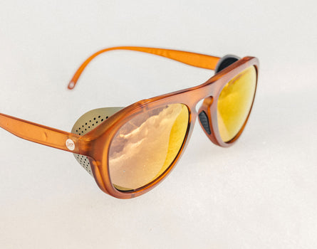 Sunglasses with orange frame and yellow-tinted lenses on a light gray background
